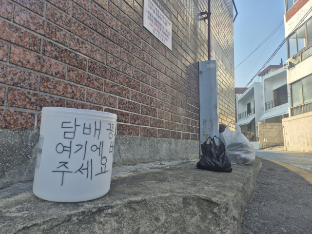 지난 12일 부산 수영구 민락로 한 다세대 주택 담벼락에 걸린 현수막(위). 인근 한 골목 귀퉁이에는 주민이 직접 마련한 담배꽁초 수거함이 놓여져 있다. 손혜림 기자