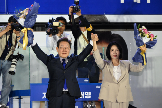 제21대 대통령 당선이 확실시되는 더불어민주당 이재명 대선 후보와 부인 김혜경 여사가 4일 서울 여의도 국회 인근에서 당 주최로 열린 국민개표방송 행사에 참석해 박찬대 상임총괄선대위원장과 정은경 총괄선대위원장단으로부터 꽃다발을 받은 뒤 시민들을 향해 두 팔을 들어 인사하고 있다. 연합뉴스