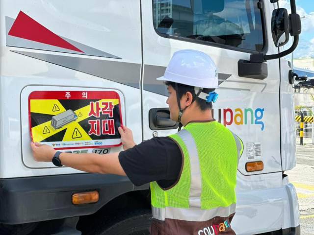 쿠팡 관계자가 대형 화물차 조수석 측면에 '사각지대 주의' 알림 표지를 부착하고 있다. 쿠팡 제공. 연합뉴스