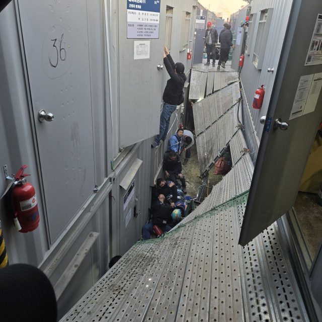 19일 울산 울주군 에쓰오일 샤힌프로젝트 공사 현장에서 컨테이너형 가설 건물을 잇는 2m 높이 비계(임시 가설물) 통로가 무너져 내렸다. 통로 바닥에 작업자들이 엉켜 있고, 한 작업자는 컨테이너 문에 매달린 채 구조를 기다리고 있다. 민주노총 전국플랜트건설노조 울산지부 제공