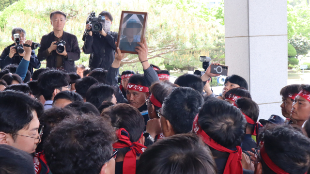 21일 오전 경남 창원시 의창구 경남경찰청 청사 앞에서 화물연대 조합원들과 경찰이 대치했다. 한 화물연대 조합원이 지난 20일 집회 중 사고로 목숨을 잃은 조합원 사진을 들고 있다. 최환석 기자